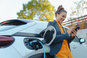 woman leaning against her electric vehicle while it is charging