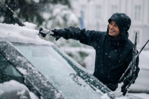 man brushing snow of his windsheild