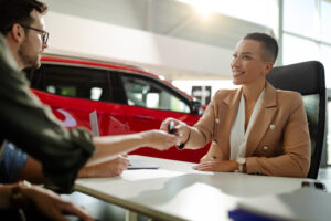 Female customer receiving car keys, shaking hands with saleswoman. Focus on saleswoman.